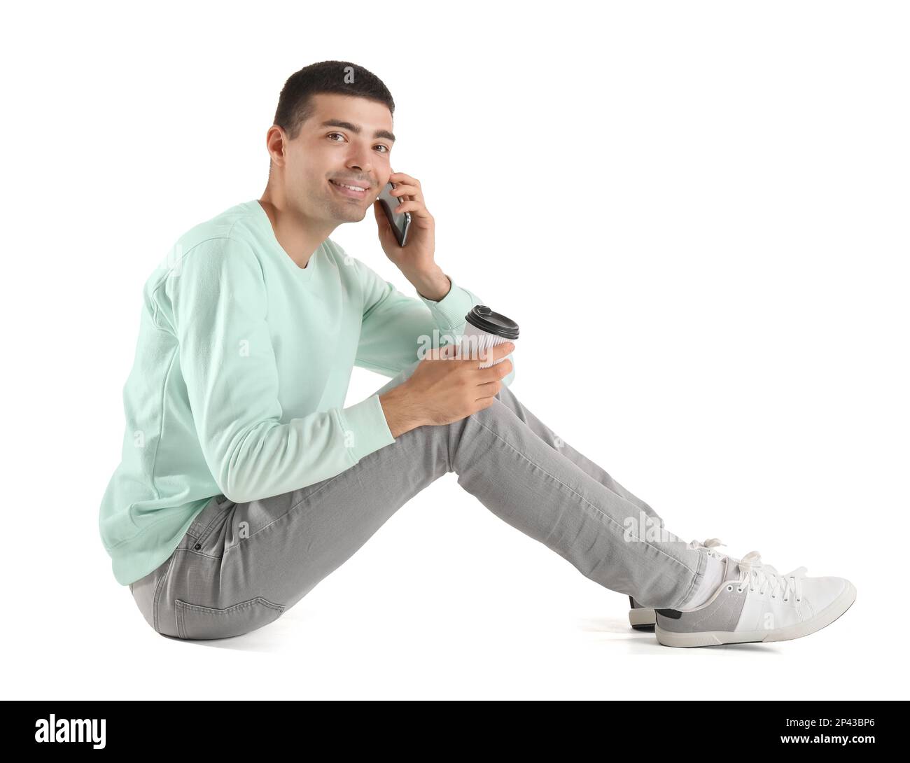 Ein hübscher Kerl mit Kaffeetasse, der mit einem Handy auf weißem Hintergrund spricht Stockfoto