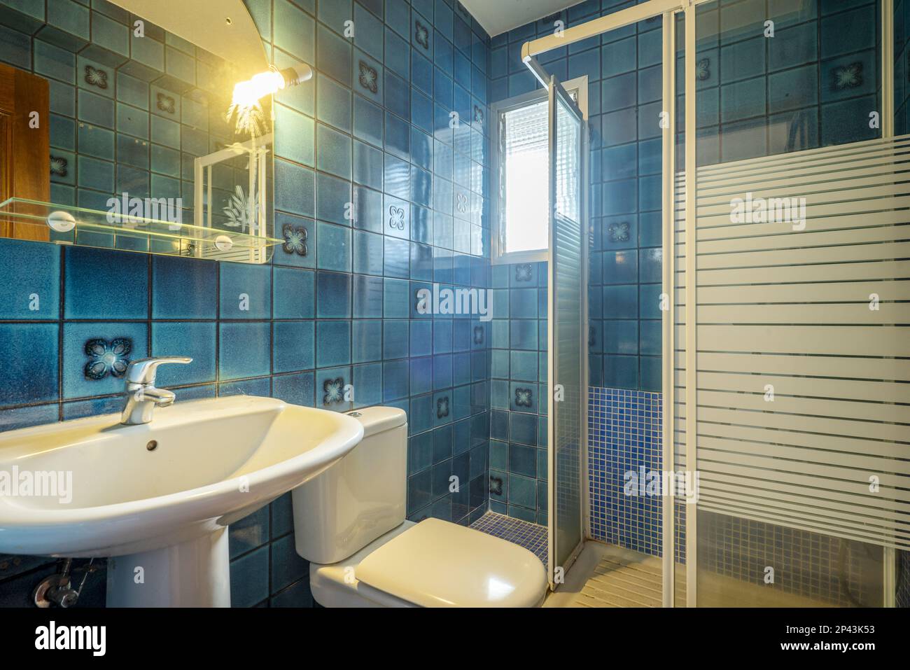 Badezimmer mit Spiegel an der Wand mit Glasregal, Porzellanwaschbecken,  quadratischer weißer Duschkabine und superalten blauen Fliesen  Stockfotografie - Alamy