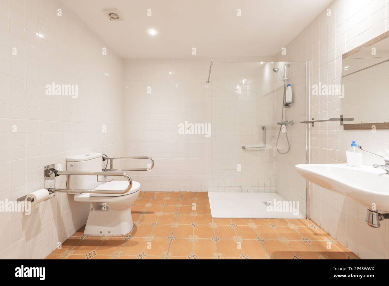 Großes Badezimmer und Porzellanwaschbecken unter einem rahmenlosen Spiegel und Duschkabine mit Bildschirm aus gehärtetem Glas und Toilette mit behindertengerechter Unterstützung Stockfoto