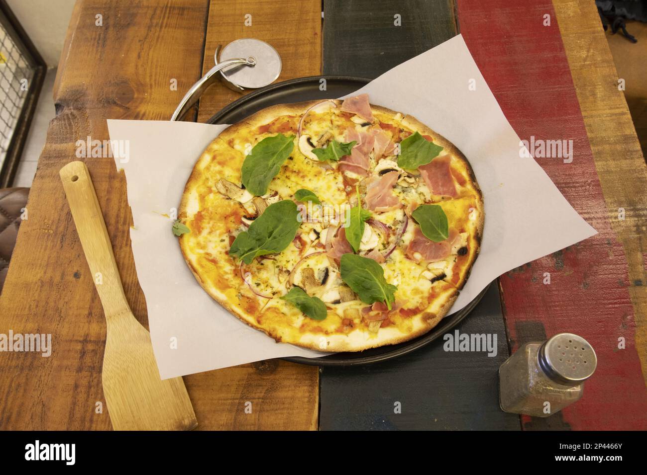 Tolle italienische Pizza mit dünner Kruste mit Pilzen, Prosciutto und viel Basilikum auf einem Holztisch Stockfoto