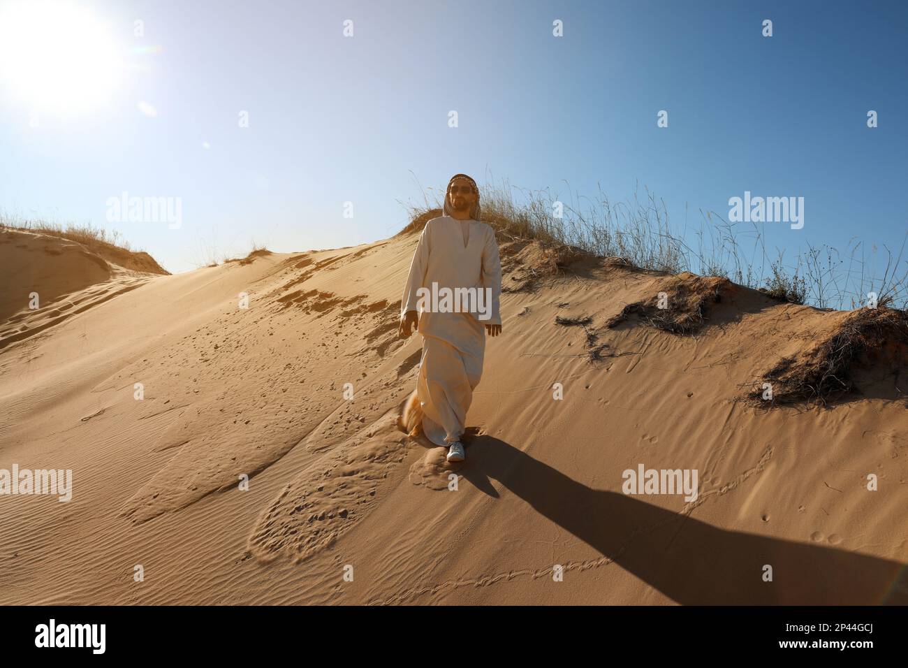 Ein Mann in arabischen Klamotten, der an einem sonnigen Tag durch die Wüste spaziert Stockfoto