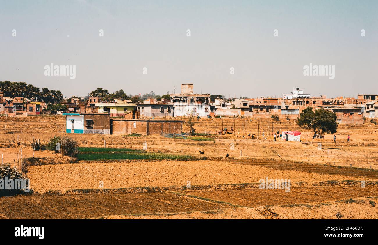 Ländliches indisches Dorf Landschaft in der Ferne mit landwirtschaftlichen Feldern im Vordergrund und blauem Himmel im Hintergrund. Stockfoto