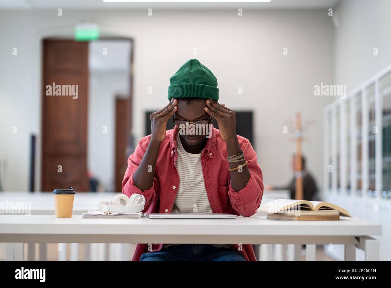 Ein müder Schwarzer, der in der Bibliothek sitzt, sich unmotiviert fühlt, zu lernen und sich zu konzentrieren. Stockfoto
