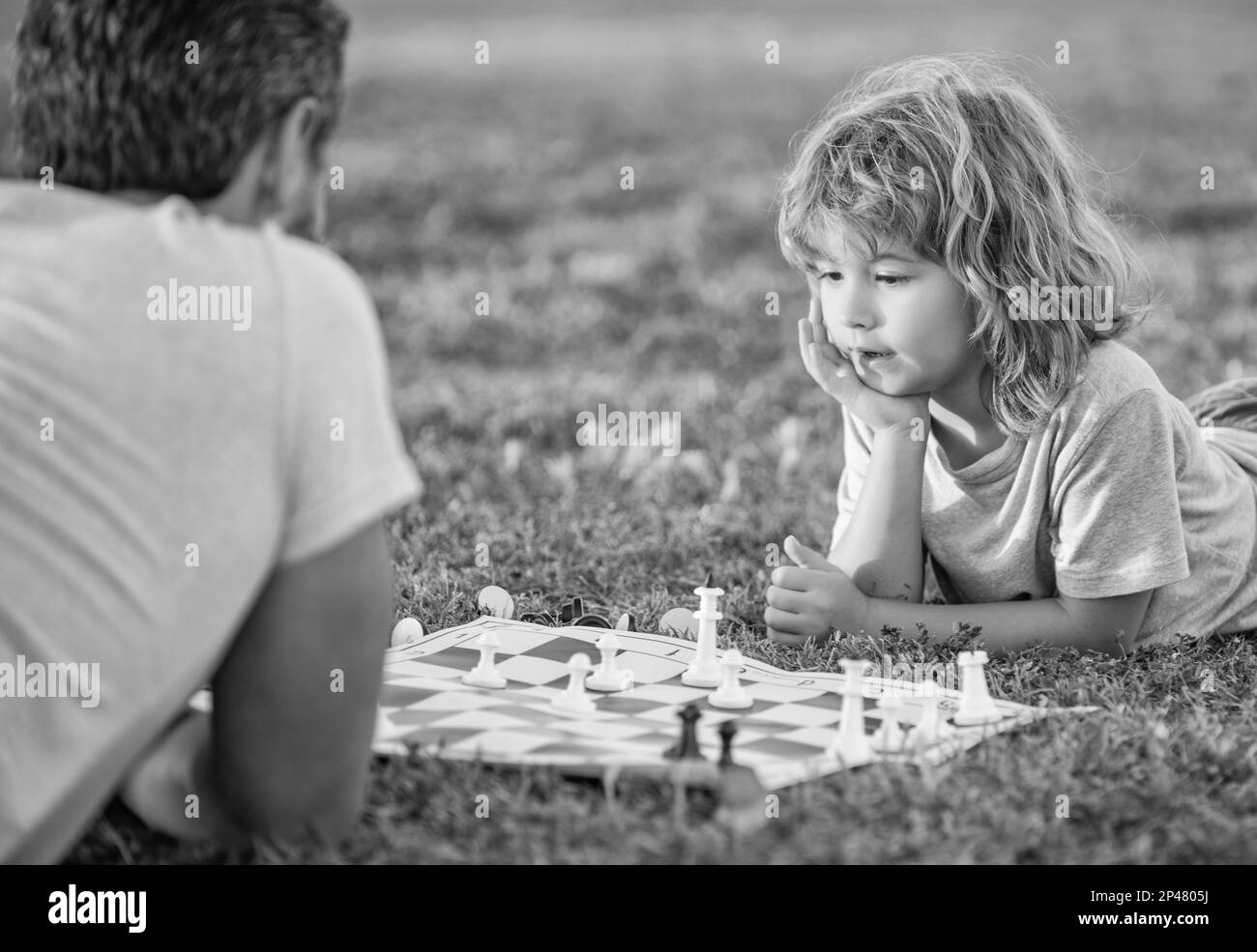 Glückliche Familie von Eltern und Sohn spielen Schach auf grünem Gras im Park im Freien, Entwicklung der Kindheit. Stockfoto