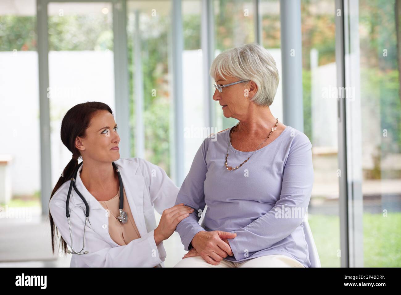 Wie fühlst du dich heute? Junge Ärztin, die sich um ihren älteren Patienten kümmert. Stockfoto