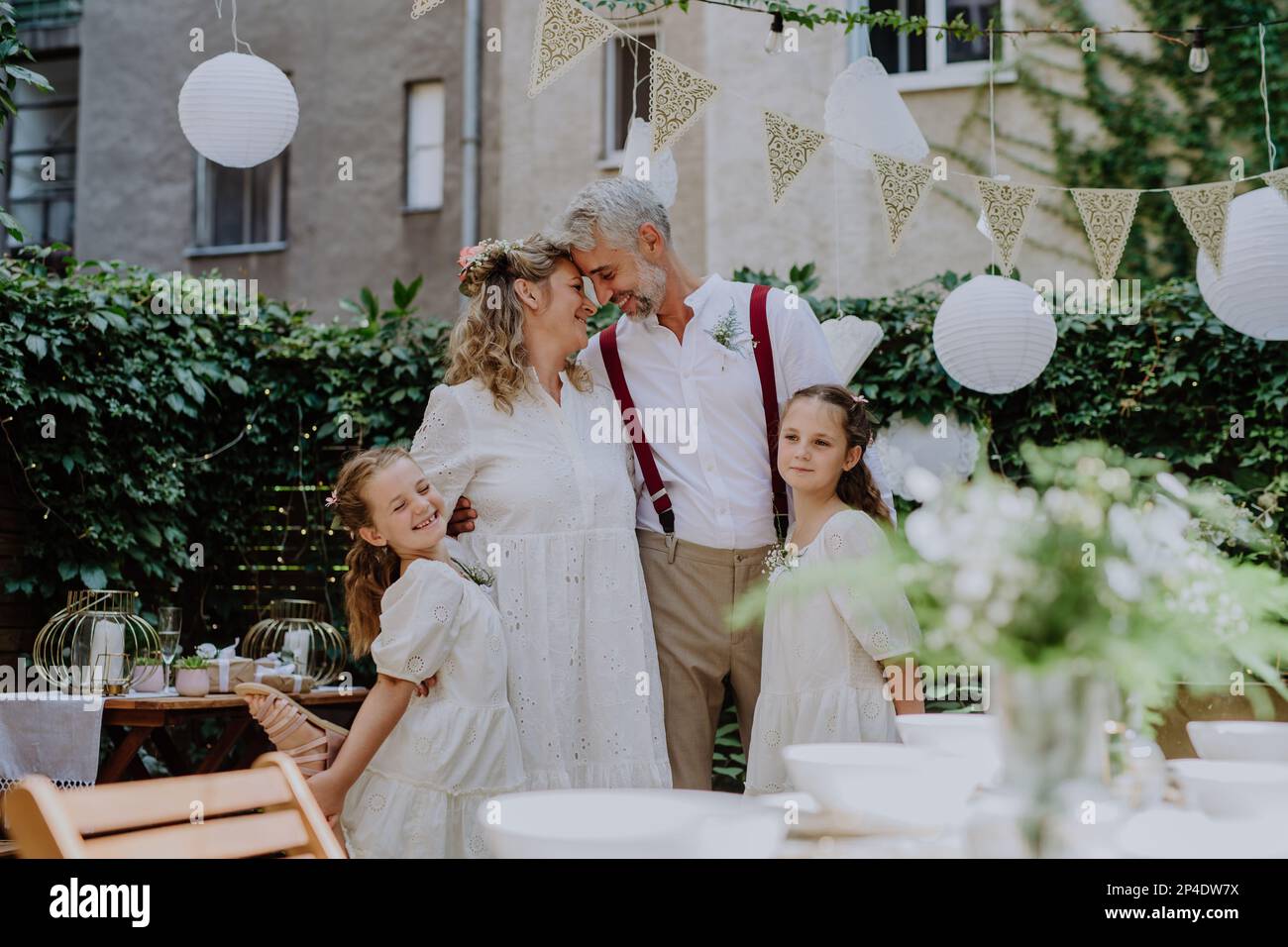 Reife Braut und Bräutigam posieren mit ihren Töchtern bei der Hochzeitsfeier draußen im Hinterhof. Stockfoto