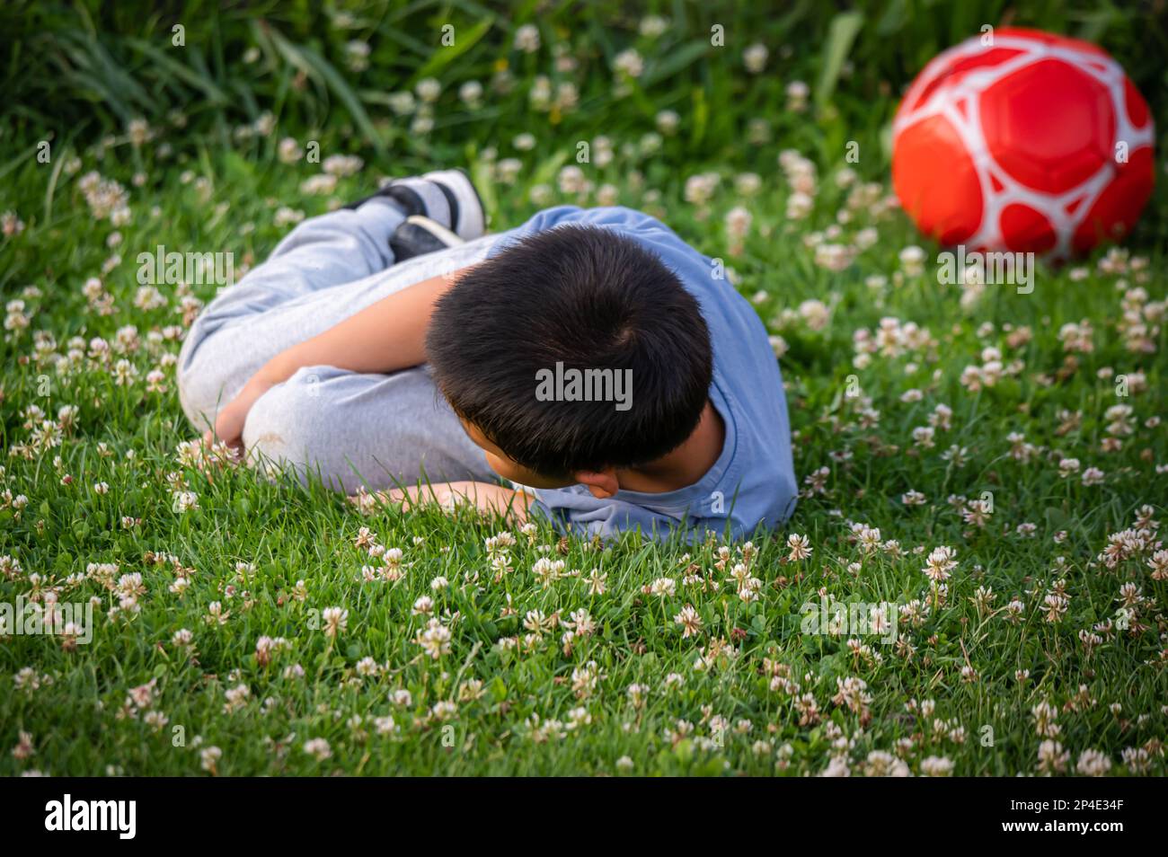 Ein Kind spielt Fußball. Ein asiatischer Junge fällt im Frühling um. Stockfoto