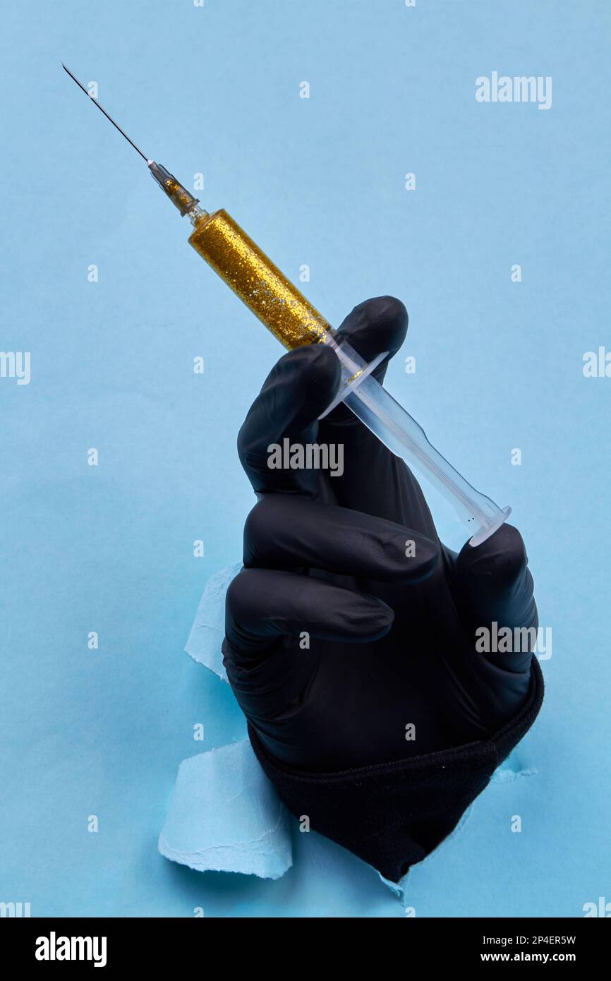 Handgehaltene Spritze mit gelbem Glitzer auf blauem Papierhintergrund. Vertikale Nahaufnahme. Stockfoto
