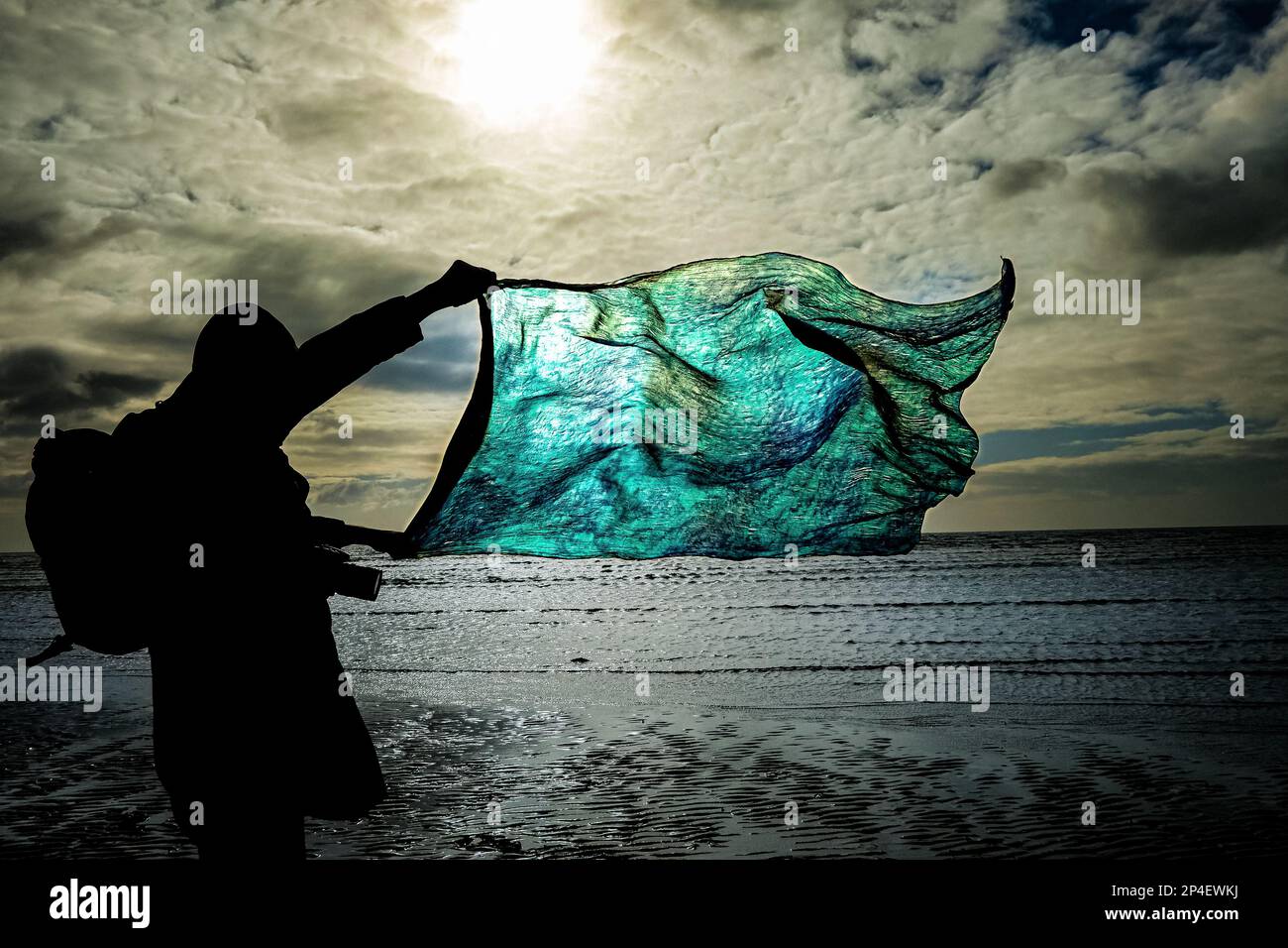 Person, die an der Küste einen blauen Schal im Wind hält. Stockfoto