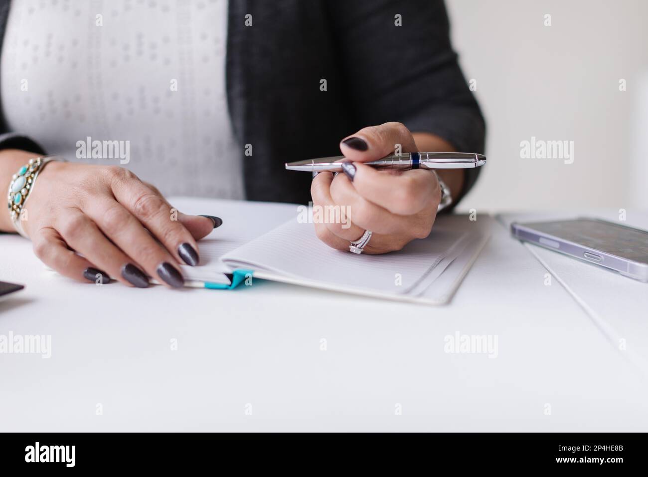 Nahaufnahme von weißen Händen mit Stift und Tagebuch am modernen Schreibtisch Stockfoto