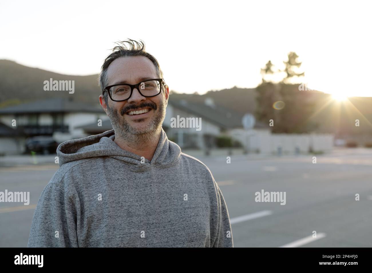 Mann mittleren Alters mit Brille lächelt draußen bei Sonnenuntergang Stockfoto