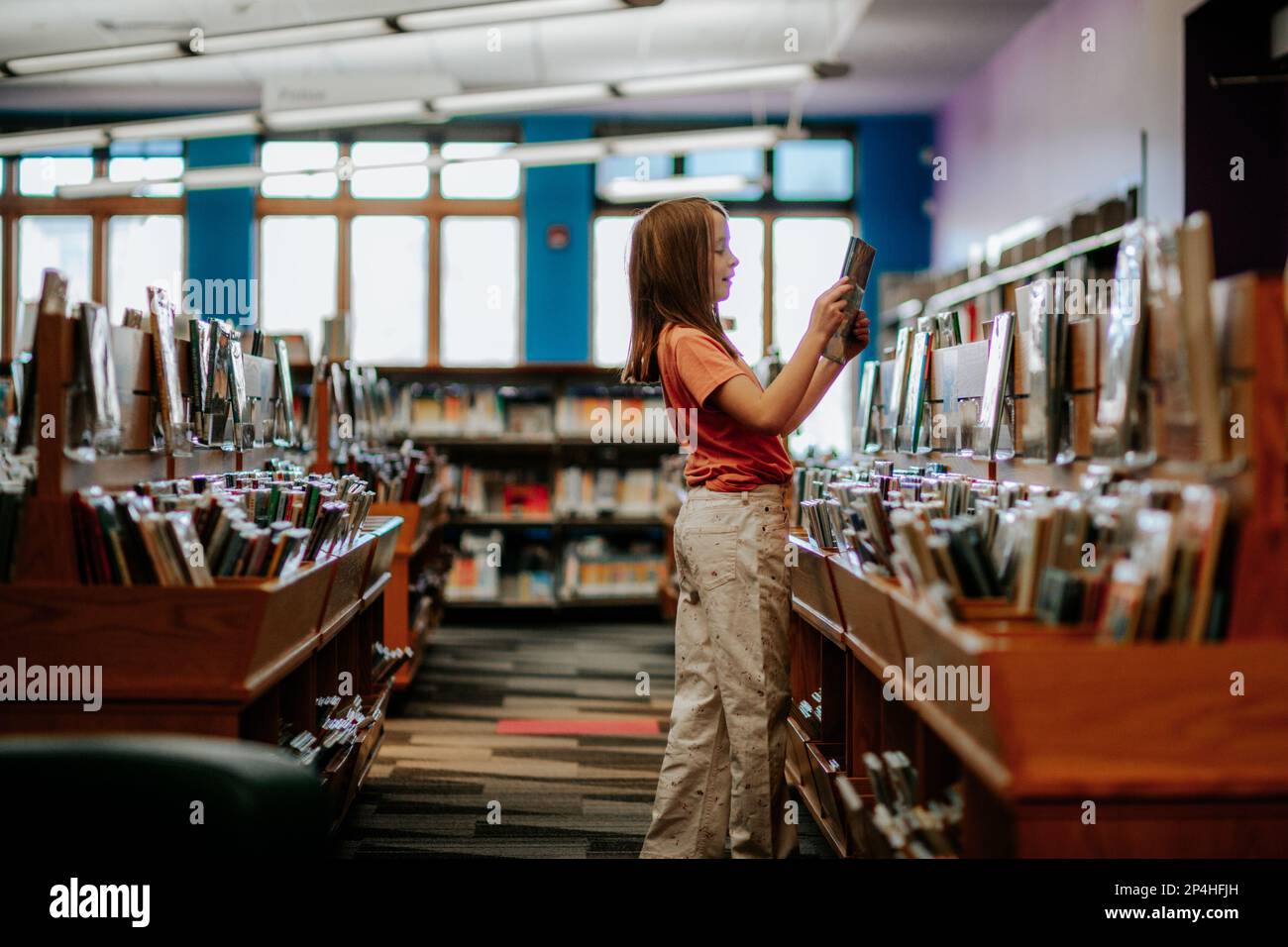 Glückliches junges Mädchen, das ein Buch in einer Bibliothek aussucht Stockfoto