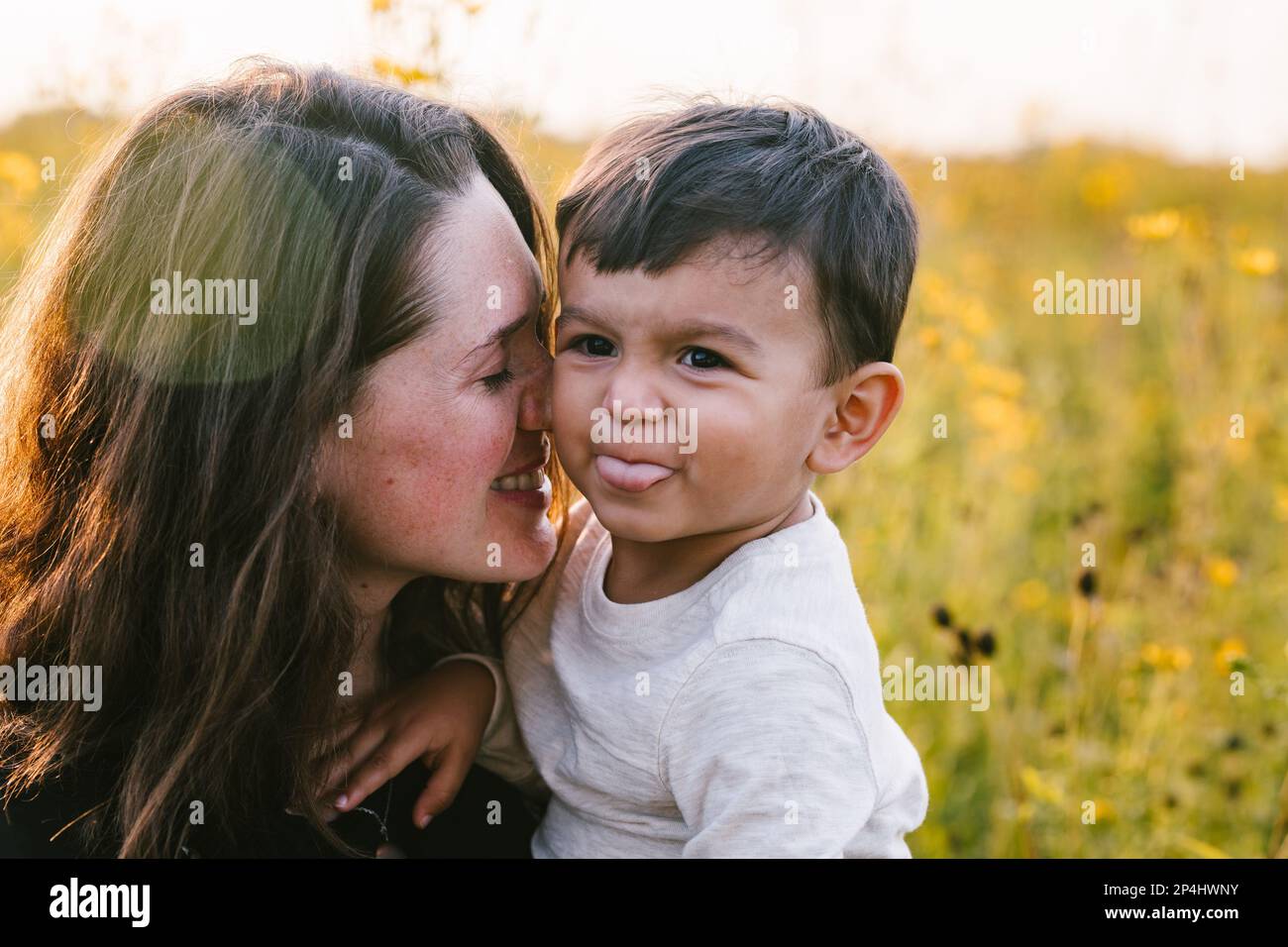 Mutter kuschelt mit Liebe an multirassischen Sohn draußen auf dem Blumenfeld Stockfoto