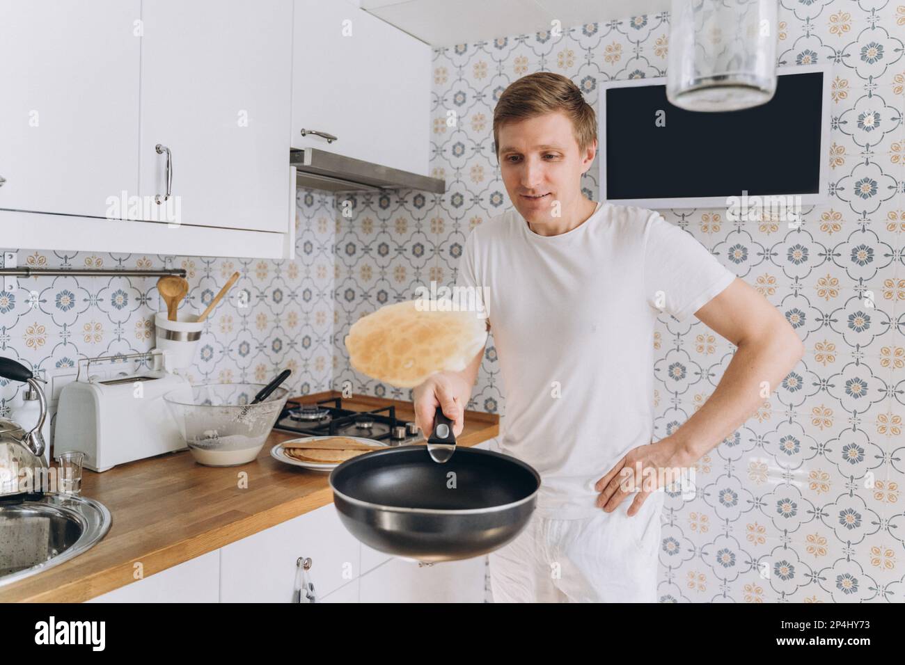 Ein Mann in weißen Pfannkuchen und wirft sie in eine Pfanne Stockfoto