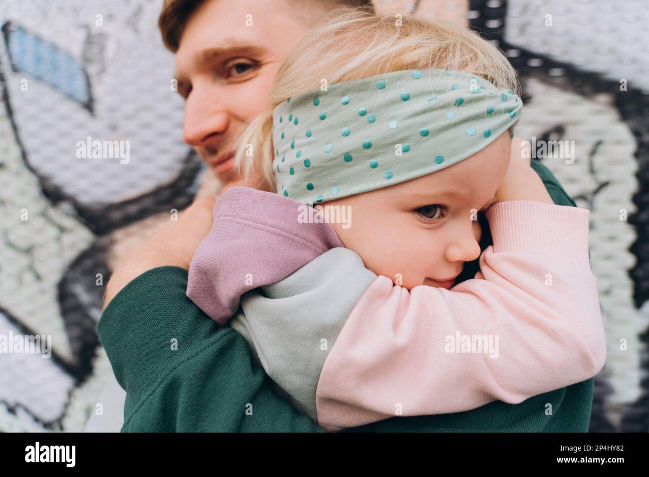 Dad in Kapuze umarmt eine zweijährige Tochter vor Graffiti Stockfoto