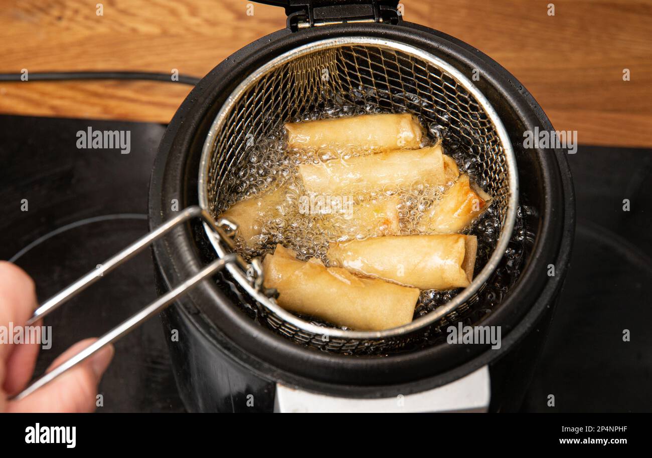 Die Herstellung von Frühlingsrollen in einem speziellen Frittiertopf. Gekochte Brötchen in sprudelndem Öl in der Hausküche. Stockfoto