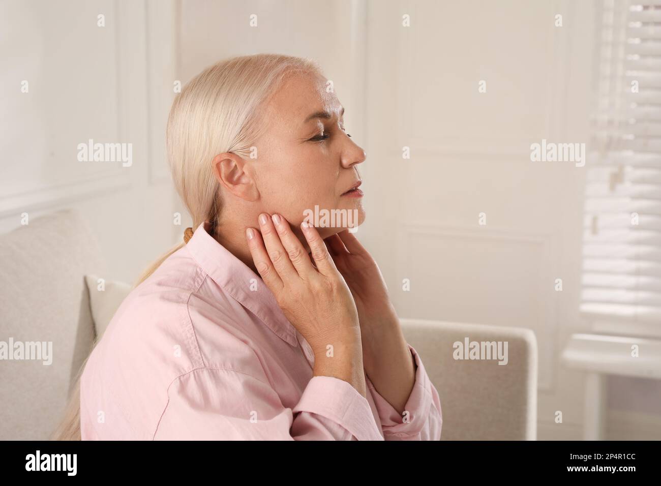 Reife Frau, die zu Hause Schilddrüsen-Selbstuntersuchung macht, Platz für Text Stockfoto