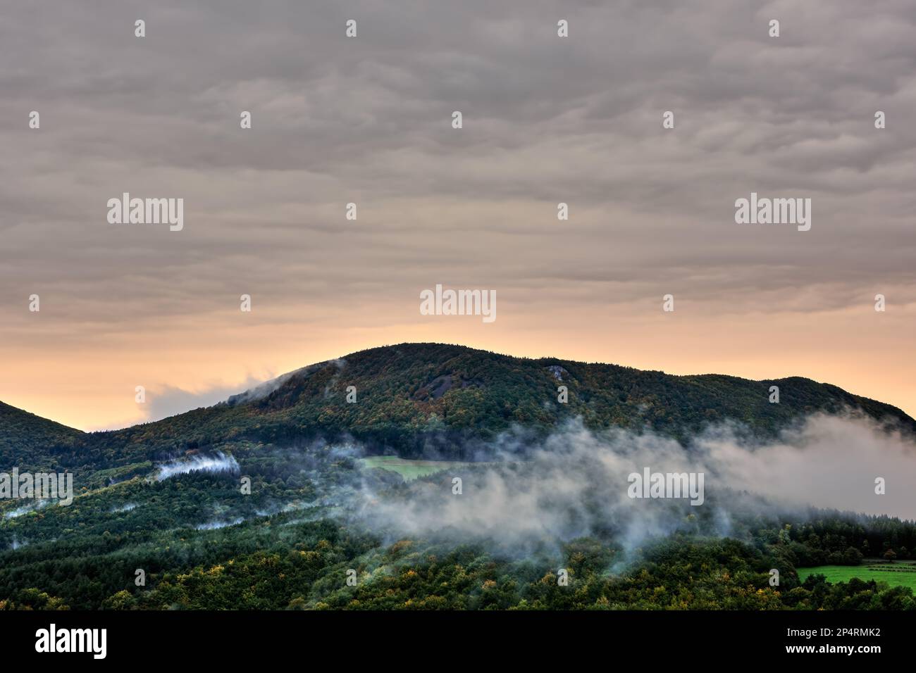 Berg mit Wald bei Sonnenaufgang, wunderschöner bunter Himmel. Neblige Landschaft. Spätherbst. Homolka, Slowakei. Stockfoto