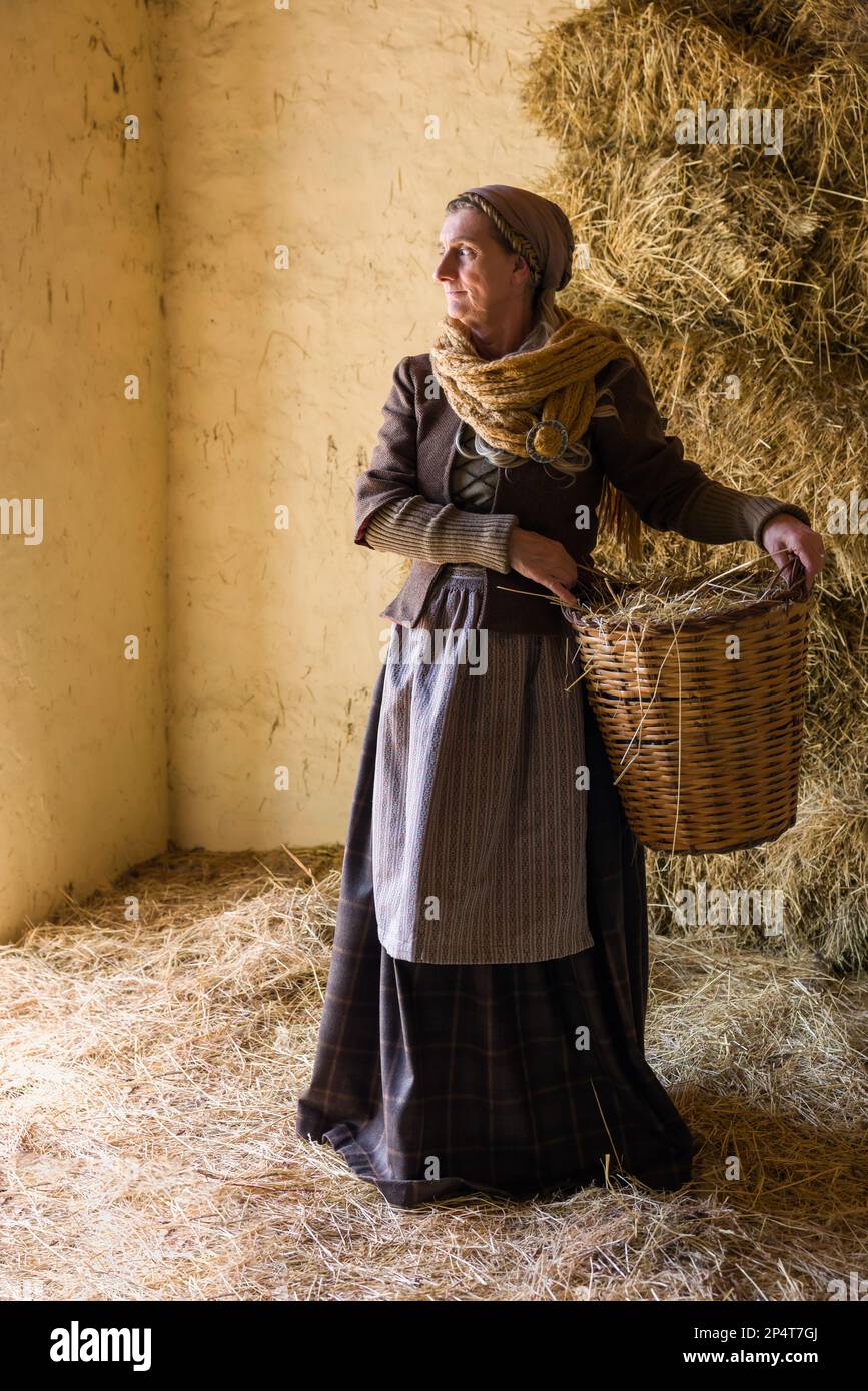 Frau in historischer mittelalterlicher Tracht posiert mit einem Weidenkorb in einer Heuscheune Stockfoto