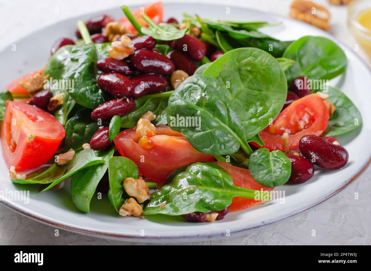 Salat aus roten Bohnen, veganer Salat mit Spinat, Kirschtomaten, Walnüssen, Bohnen und Senfkresse auf hellem Hintergrund Stockfoto