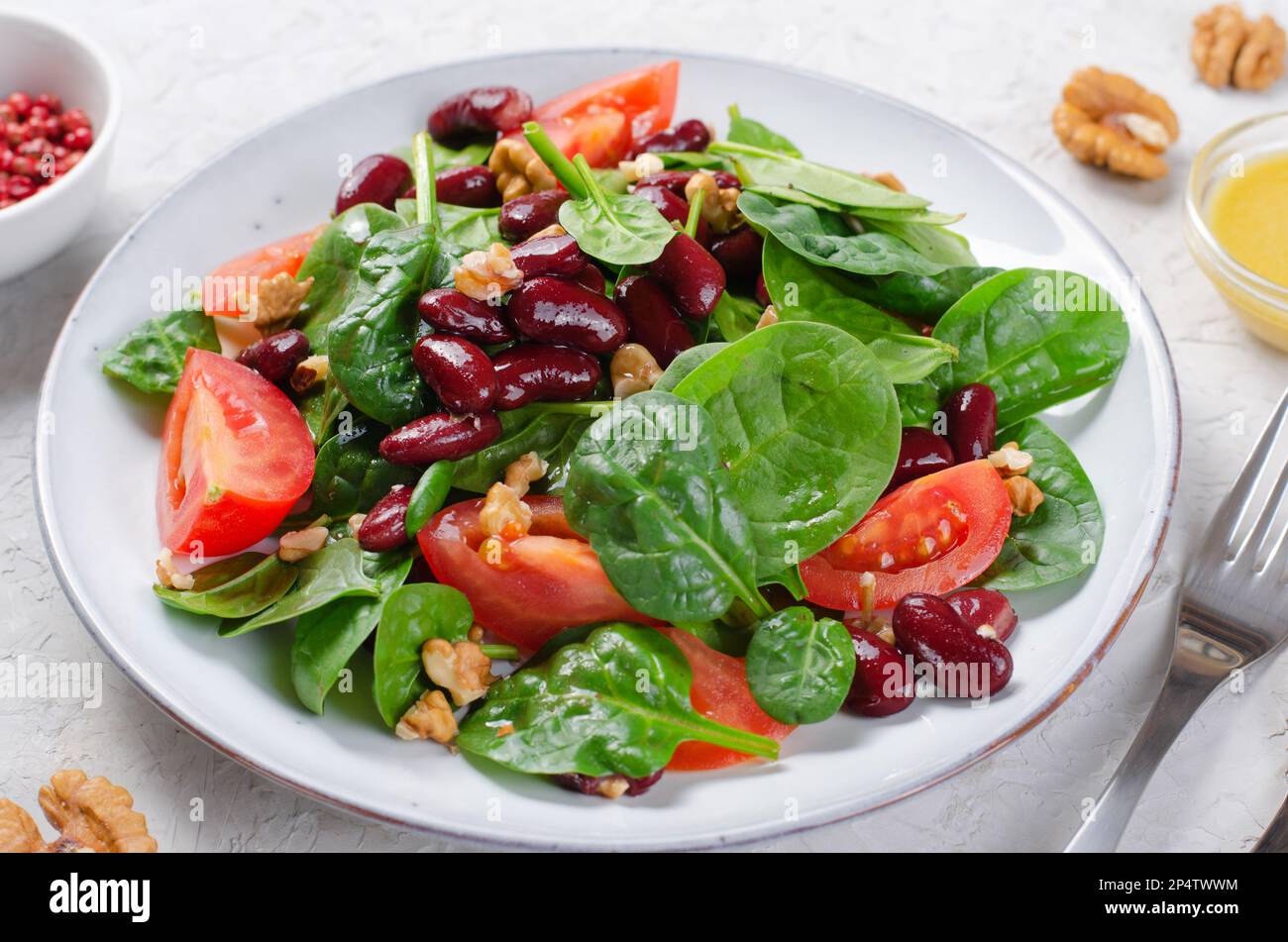 Salat aus roten Bohnen, veganer Salat mit Spinat, Kirschtomaten, Walnüssen, Bohnen und Senfkresse auf hellem Hintergrund Stockfoto