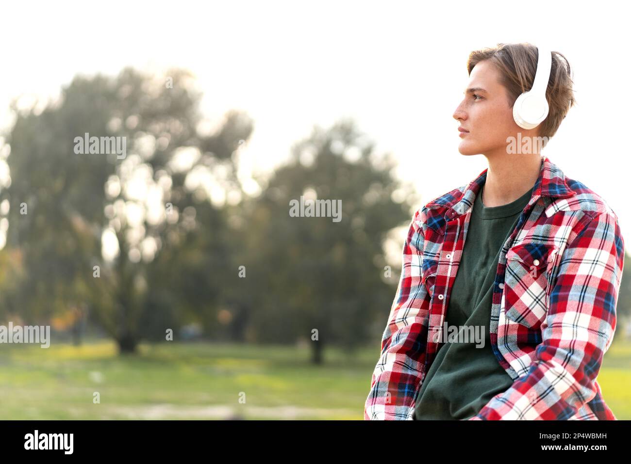Porträtfrau mit kurzen Haaren, die ein kariertes Hemd und Kopfhörer im Freien trägt. Stockfoto