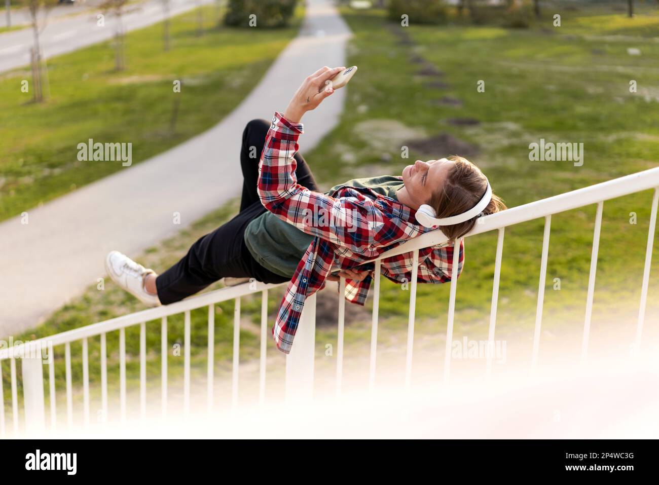 Eine Frau, die auf dem Geländer liegt und draußen im Park Musik hört. Stockfoto