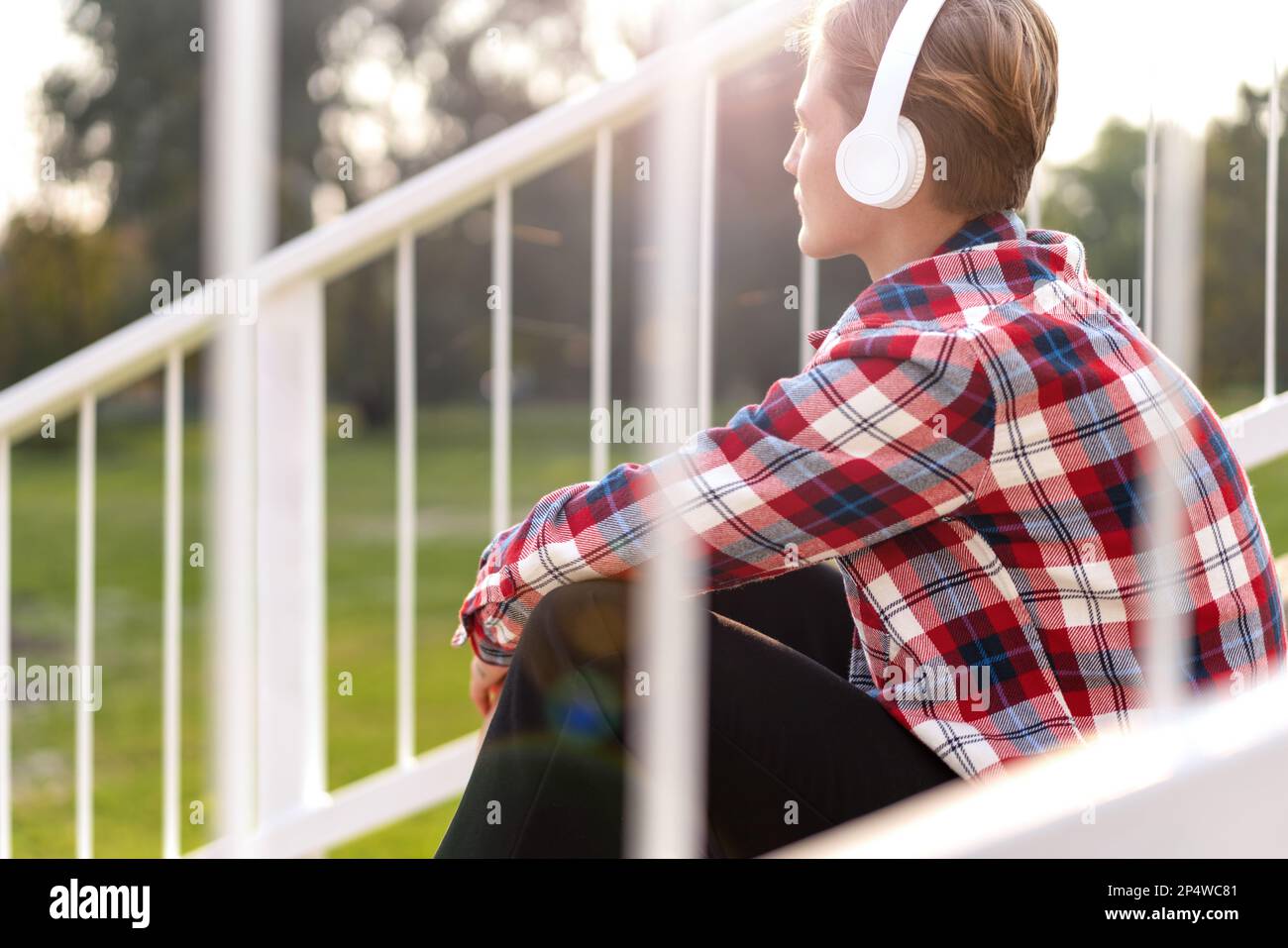 Frau mit kurzen Haaren in Kopfhörern sitzt auf einer Treppe in der Stadt und hört Musik. Stockfoto