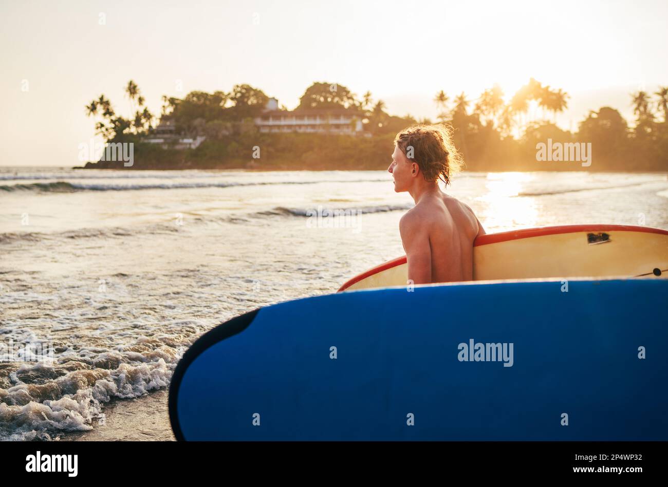 Junger Teenager mit altem Surfbrett geht zum Surfen ans Meer. Er genießt ein wunderschönes Sonnenlicht am Dewata-Strand auf Sri Lanka. Aktive Sportvakua Stockfoto