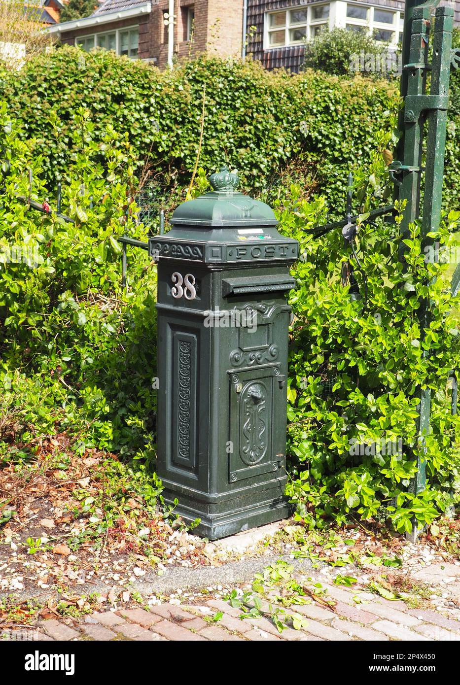 Ein schwarzer Briefkasten vor einem Hintergrund aus üppig grünen Büschen und Sträuchern, am Rande einer Straße Stockfoto