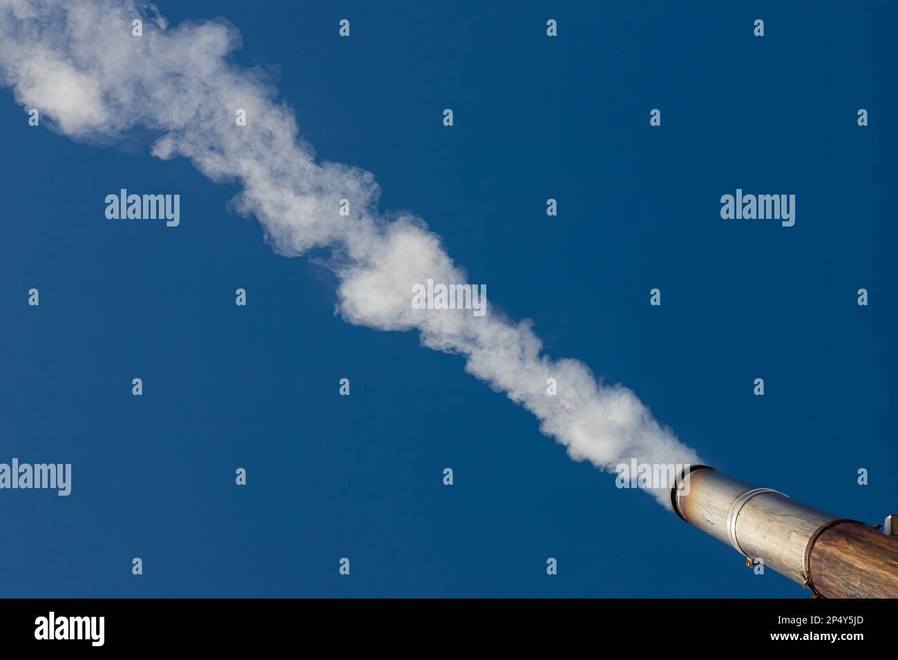 Eine Rauchfahne oder Dampf aus einem industriellen Schornstein an einem klaren blauen Himmel. Stockfoto