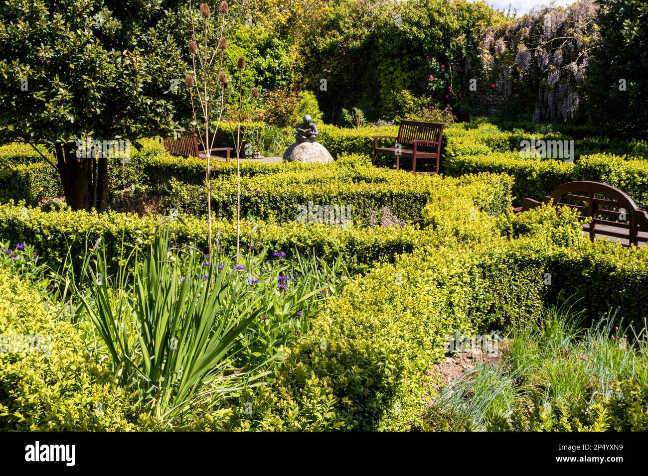 Ruhe und Frieden: Spring View of the Secret Memorial Garden, mit Bänken und der Memorial Statue of a Boy Reading, Great Torrington, Devon, Großbritannien. Stockfoto