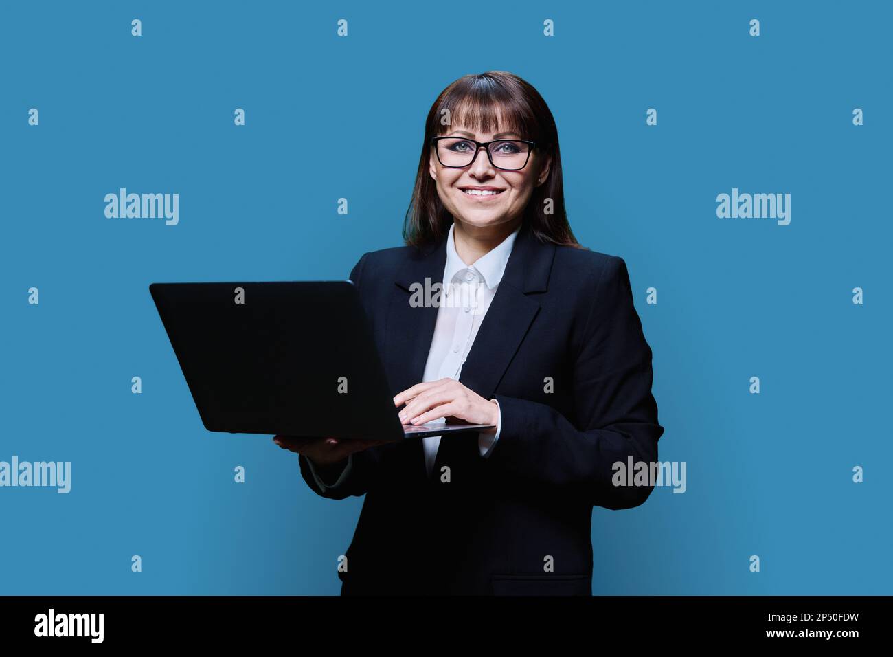 Reife Geschäftsfrau, die mit einem Notebook auf blauem Studiohintergrund posiert Stockfoto