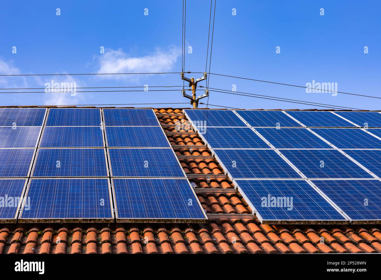 Solanpanels einer Photovoltaik-Anlage auf einem privaten Dach mit Strommast und Stromkabeln Stockfoto