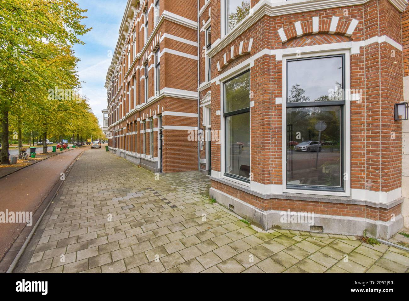 Amsterdam, Niederlande - 10. April 2021: Ein Backsteingebäude an der Seite einer Straße mit Autos, die vor dem Hotel geparkt sind und hinter denen Bäume den Bürgersteig säumen Stockfoto