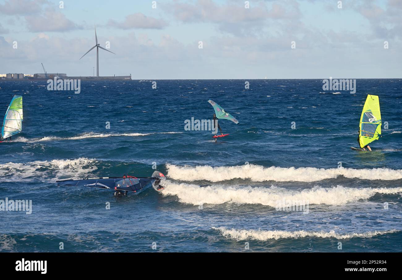 Windsurfer, einer mit Tragflächenboot, Windturbinen hinter dem Meer am Strand bei Pozo Izquierdo, Gran Canaria Stockfoto