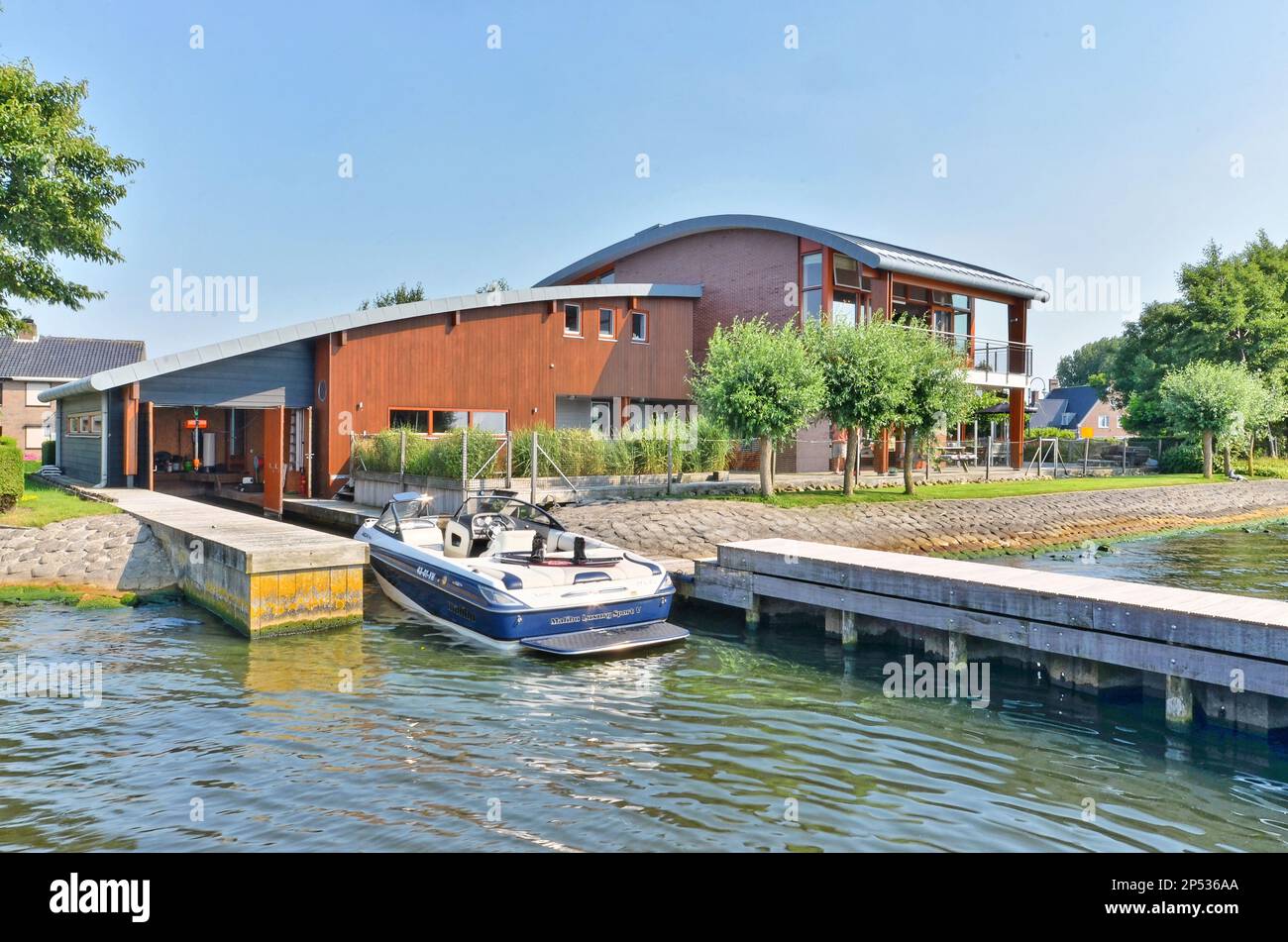 Ein Haus auf dem Wasser mit einem Boot, das an seinen Dock gefesselt ist, und zwei Häuser im Hintergrund Stockfoto