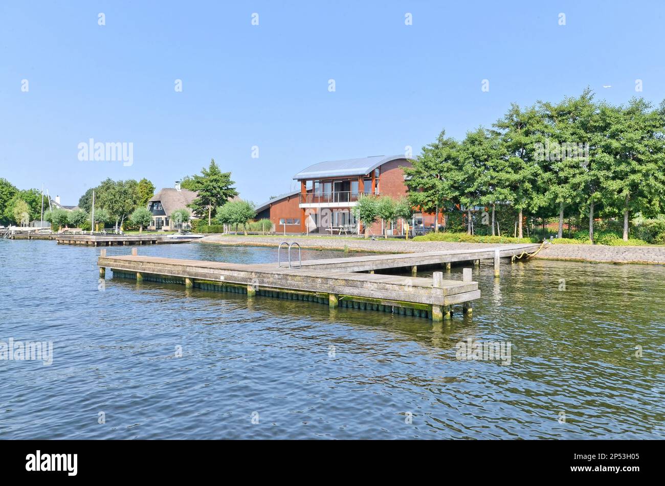 Eine Bootsanlegestelle in der Mitte eines Sees mit Häusern auf beiden Seiten und Bäumen, die das Ufer dahinter säumen Stockfoto