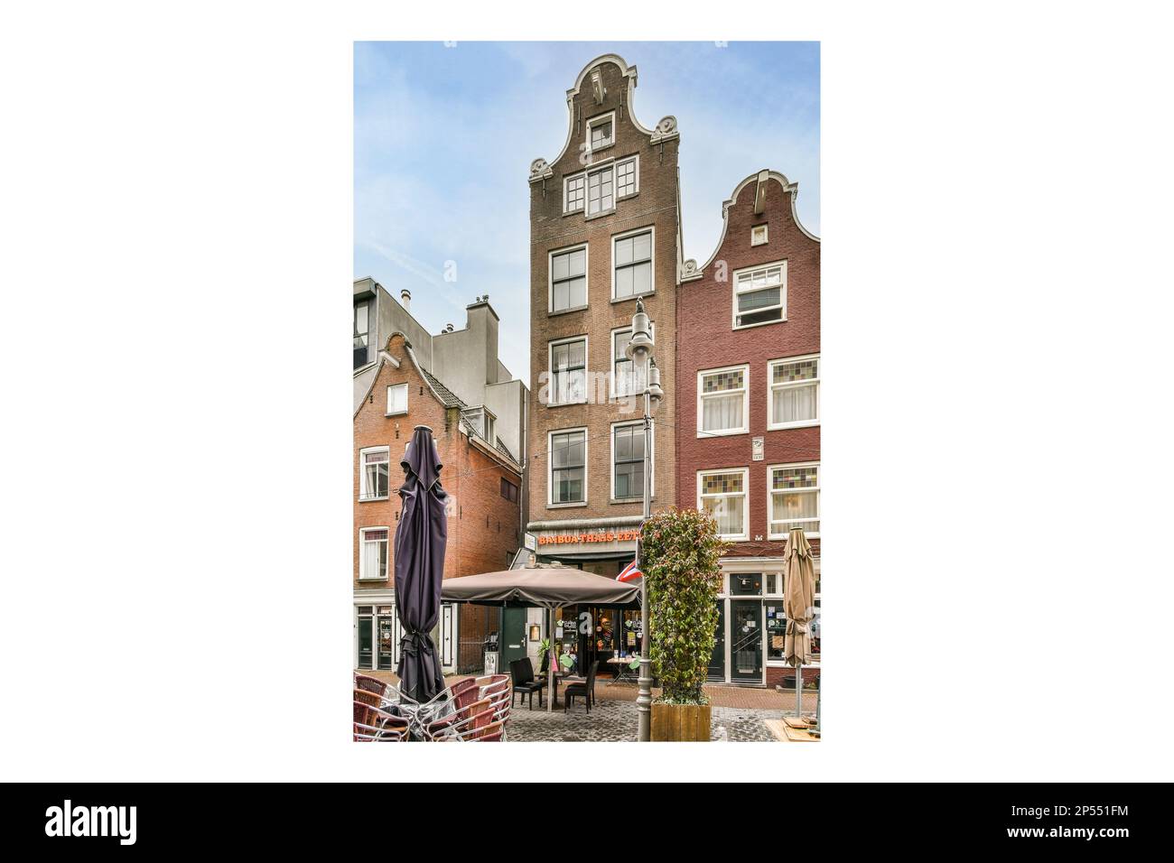 Amsterdam, Niederlande - 10. April 2021: Ein Gebäude mit einer Uhr auf der Seite und Menschen, die an einem Tisch im Freien davor sitzen Stockfoto