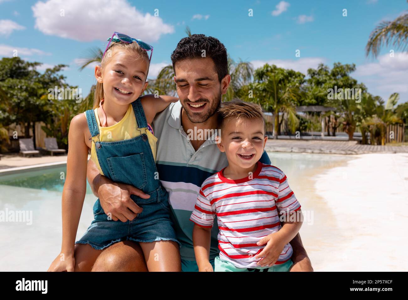 Porträt eines glücklichen birassischen Vaters und Kinder, die am Swimmingpool umarmten Stockfoto