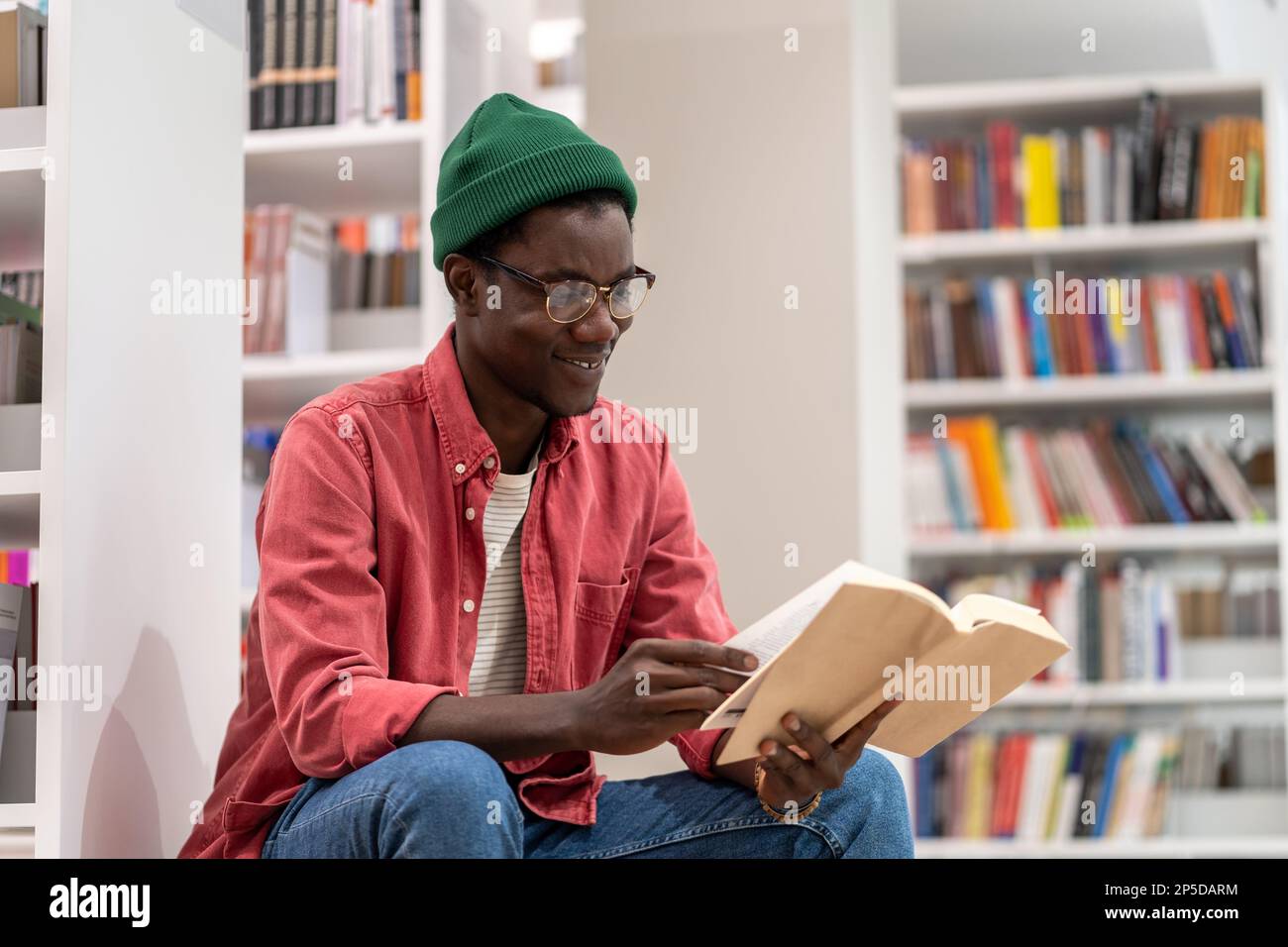 Interessierter afroamerikanischer Student liest Buch in der Universitätsbibliothek, studiert für die Prüfung. Stockfoto