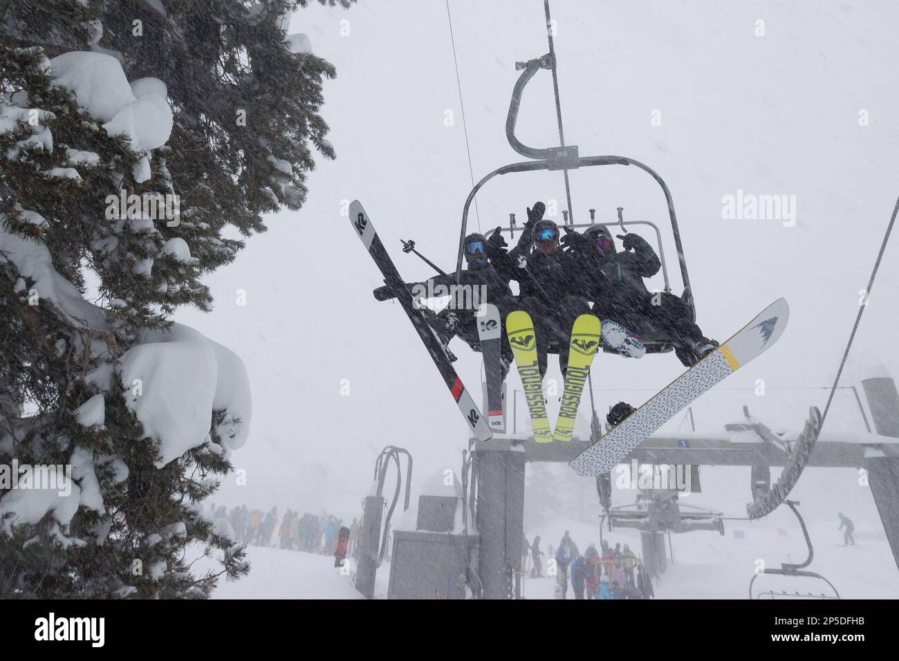 Zwei Skifahrer und ein Snowboarder fahren während eines Schneesturms im Skigebiet Mammoth Mountain mit dem Lift. Stockfoto