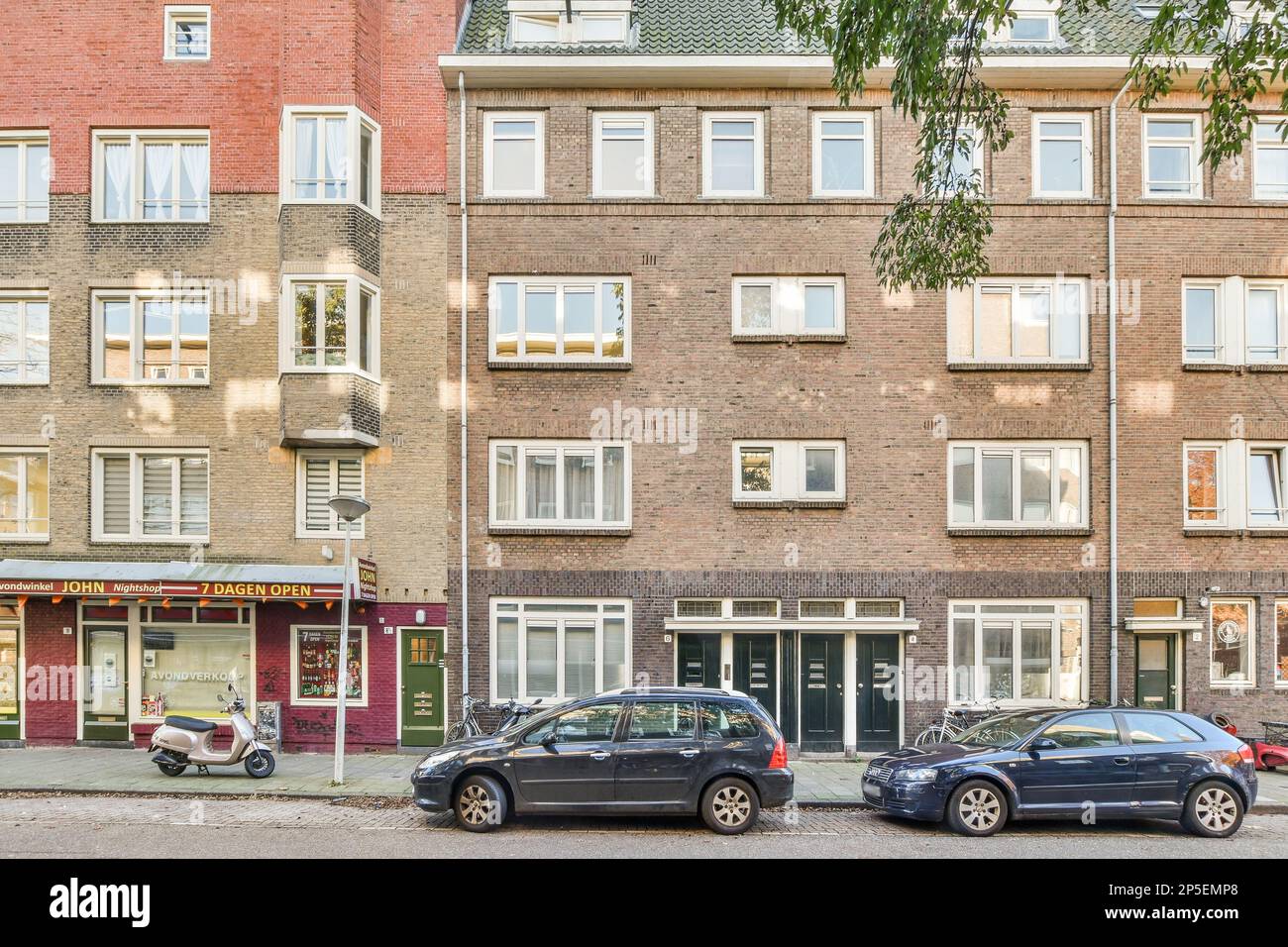 Zwei Autos parkten vor einem Wohnhaus auf der Seite einer Straße mit Bäumen und Gebäuden dahinter Stockfoto