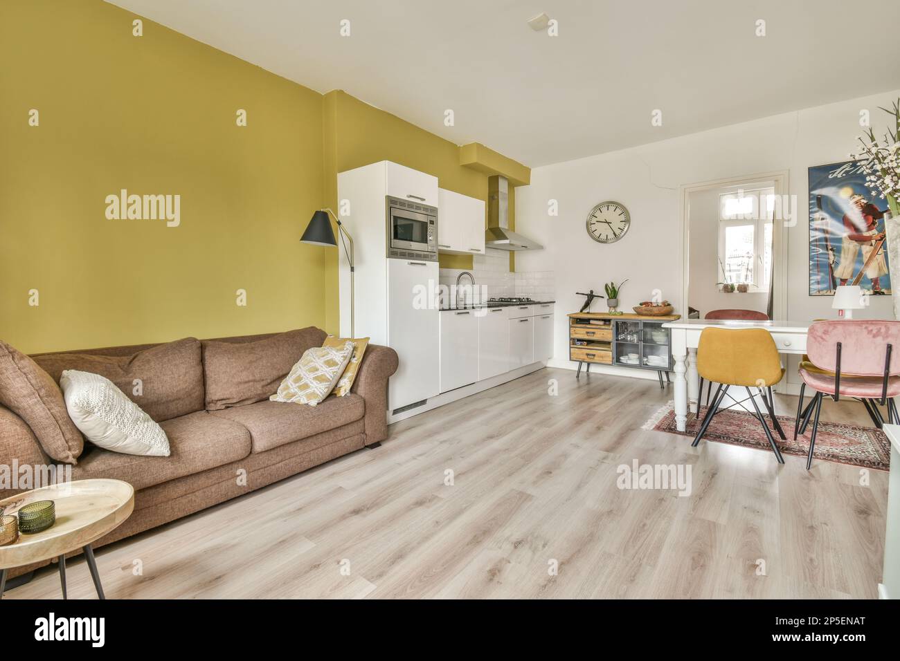 Ein Wohnzimmer mit gelben Wänden und Holzfußboden, einschließlich einer braunen Couch und zwei Stühlen in der Mitte des Zimmers Stockfoto
