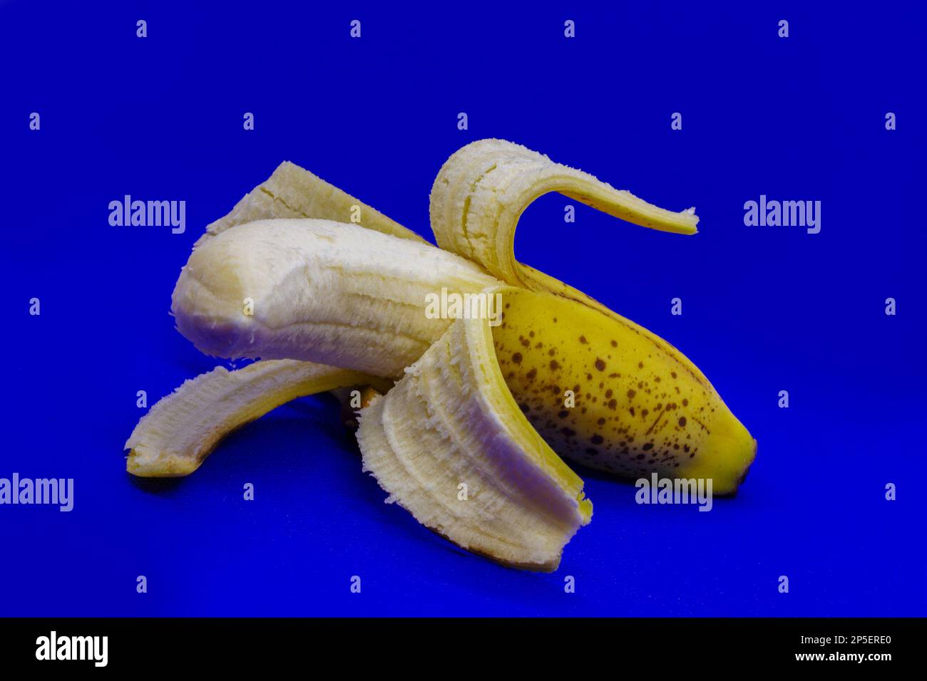 Halbgeschälte Banane auf blauem Hintergrund Stockfoto
