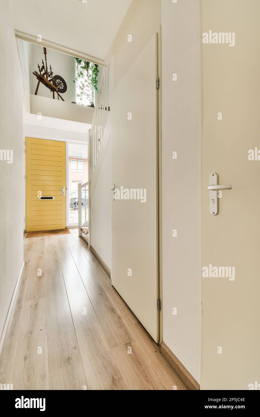 Das Innere eines Hauses mit Holzfußboden und weißen Wänden, eine offene Tür führt zu einer hellgelben Vordertür Stockfoto