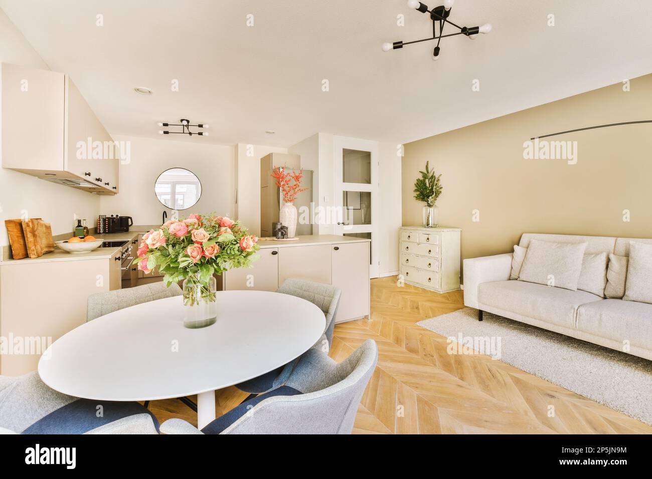 Ein Wohnzimmer mit einer weißen Couch und einem runden Esstisch in der Mitte des Zimmers ist eine offene Küche Stockfotografie