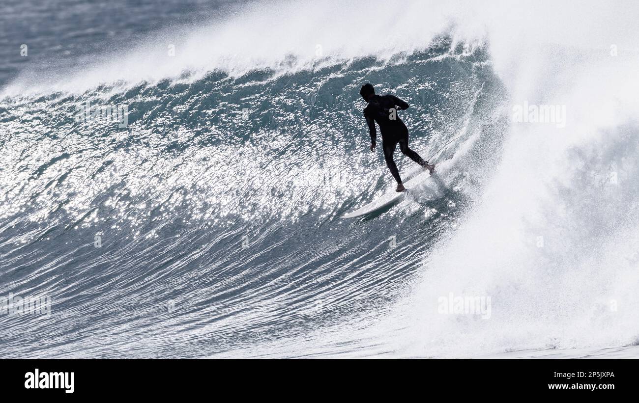 Surfer, der in der Kapuze und im Neoprenanzug nicht mehr zu erkennen ist, mit sepiakfarbenen Fotos auf kalten, windigen Meereswellen Stockfoto