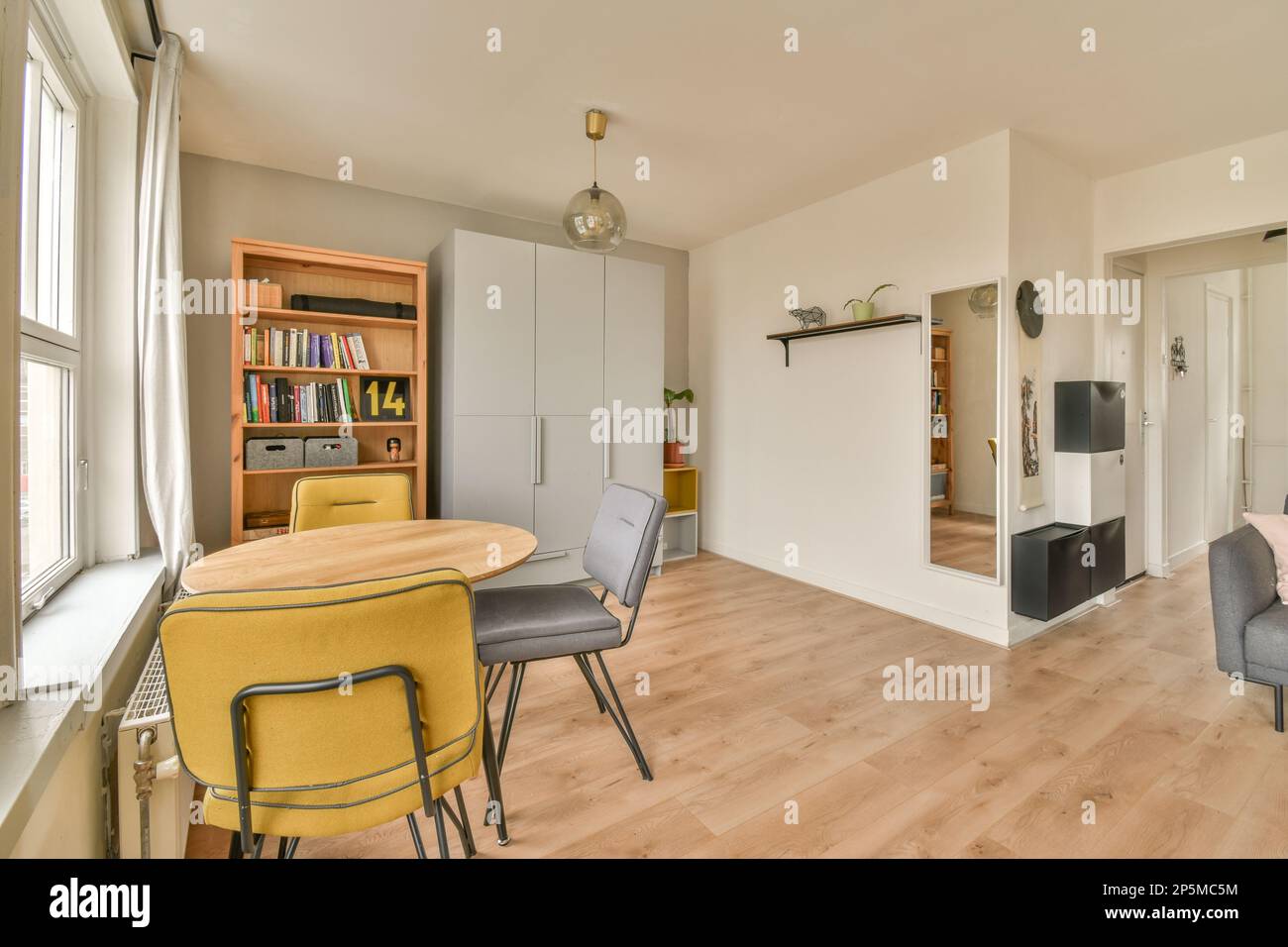 Ein Wohnzimmer mit Holzfußboden und weißen Wänden, es gibt einen gelben Stuhl vor dem Tisch Stockfoto