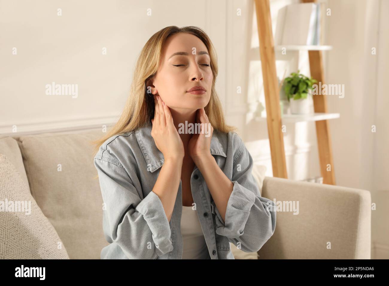 Junge Frau, die zu Hause eine Schilddrüsen-Selbstuntersuchung macht Stockfoto